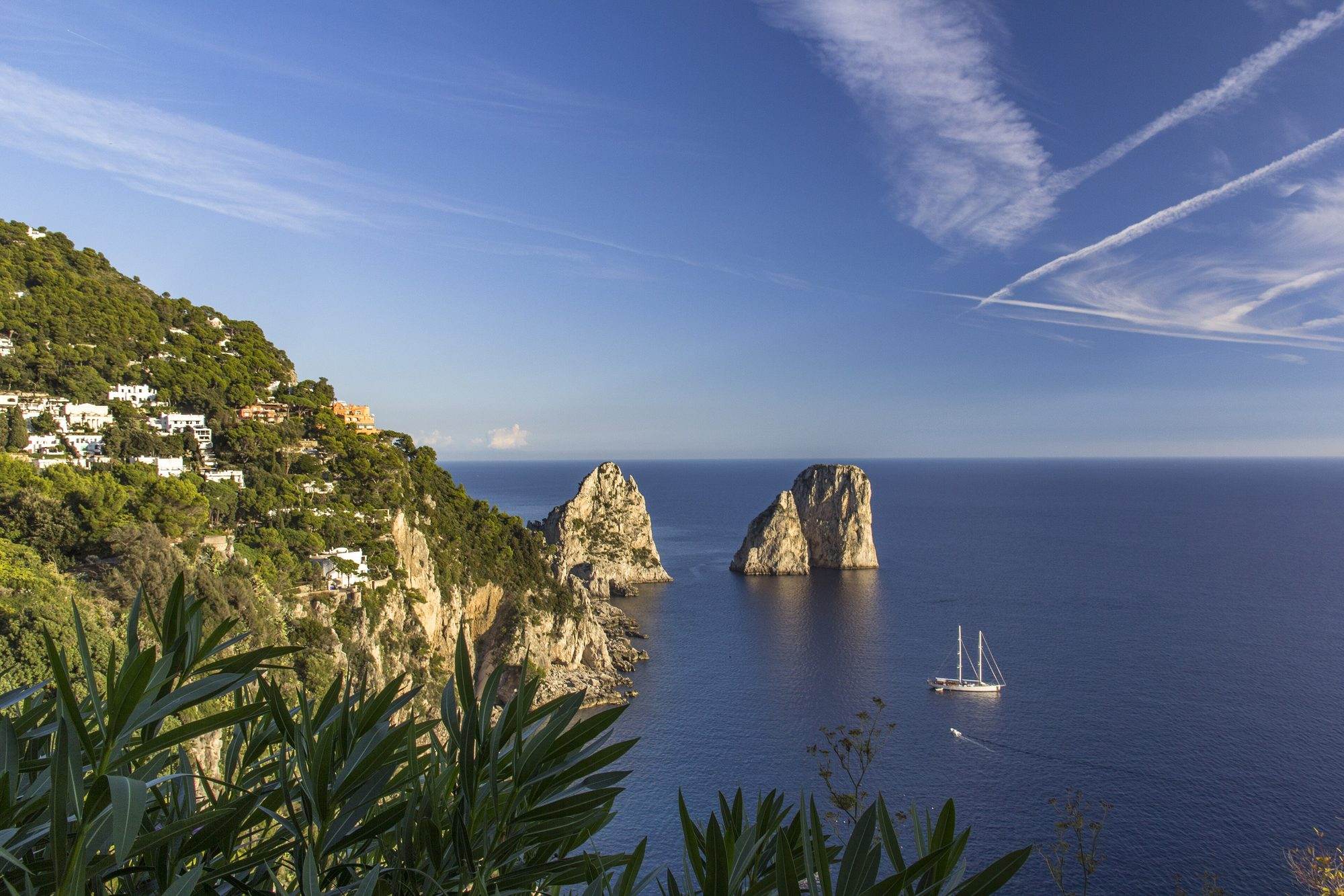 The Faraglioni of Capri seen from the sea with a sailing boat passing the rocks