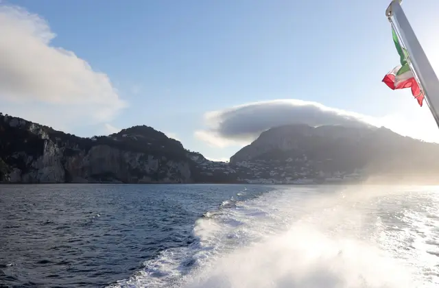 A catamaran sailing off Capri with sails up and the coastline behind